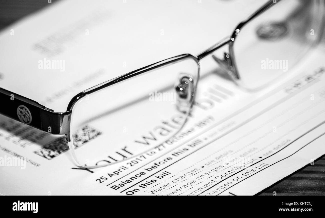 A pair of DNKY reading glasses placed on top of a water bill. Black & white image. Stock Photo