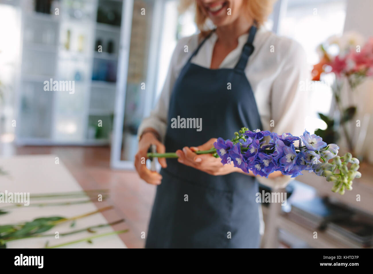 Female florist creating bouquet of flowers. Woman florist cutting flowers with scissors and designing bouquet at workshop. Focus on flowers. Stock Photo