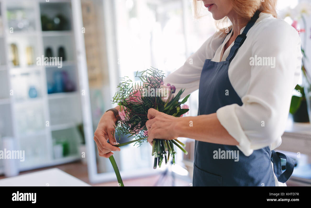 Skillful female florist creating bouquet of flowers. Young woman florist arranging flowers at workshop. Stock Photo