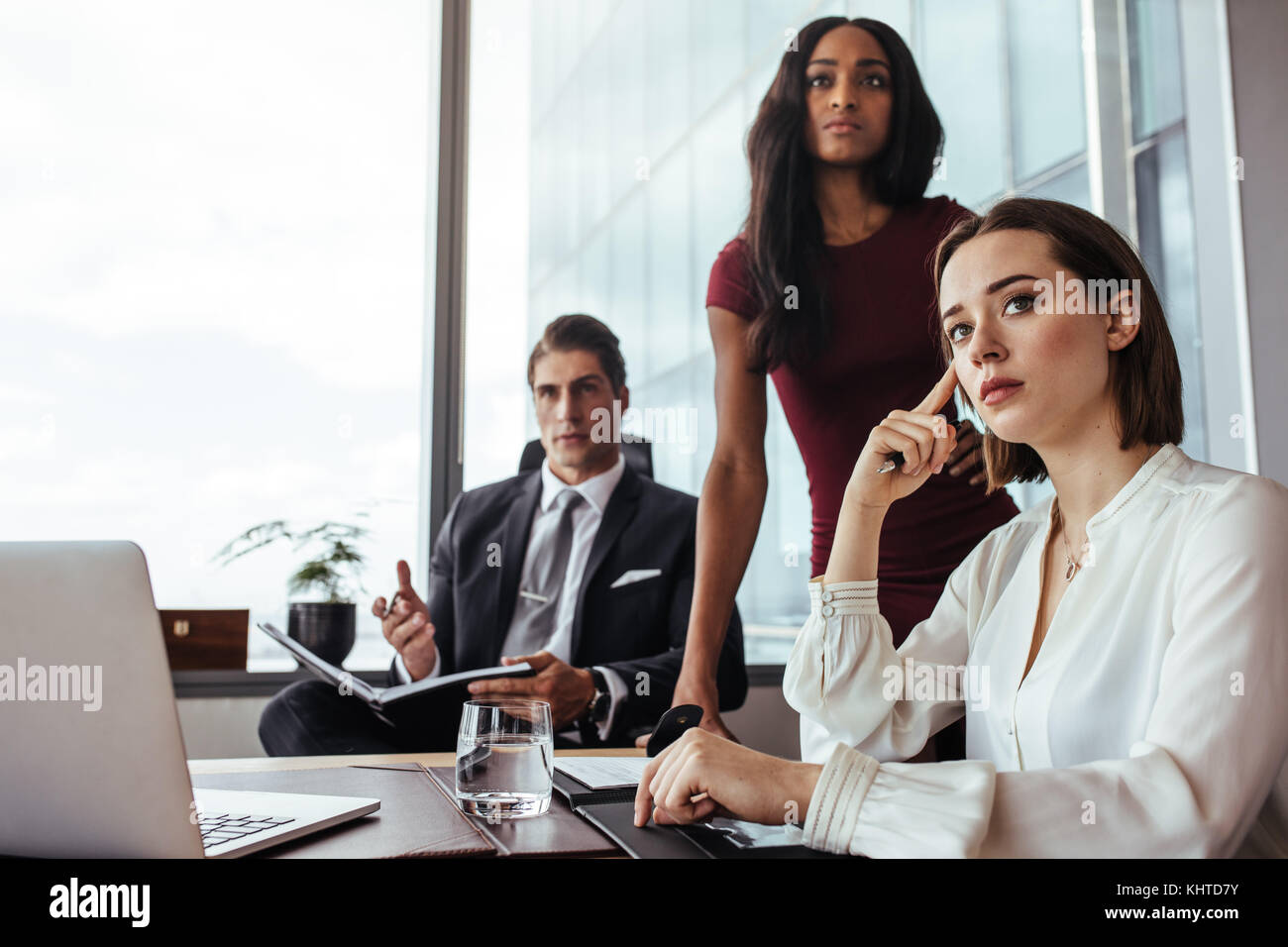 Three businesspeople sitting at desk and paying attention to something important. Young woman with colleagues during a meeting in office. Stock Photo