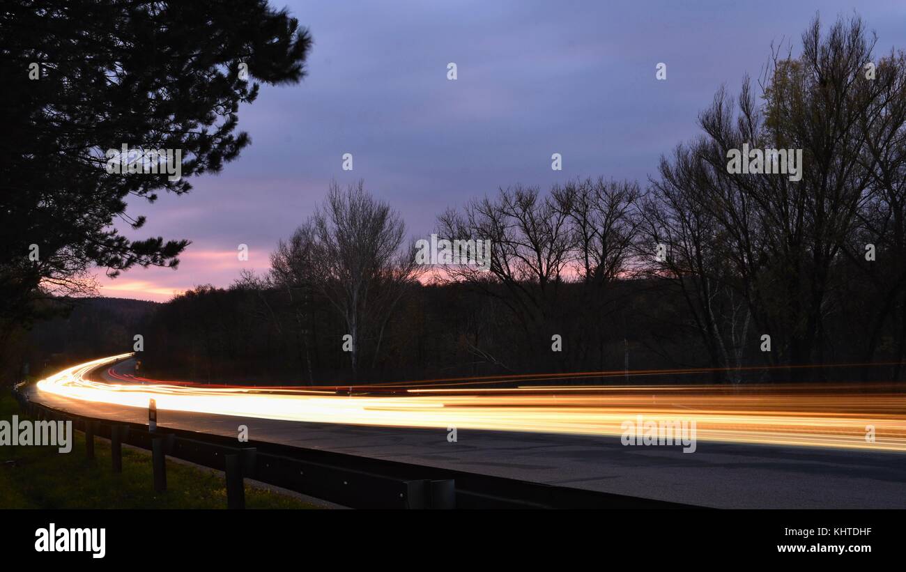 Night photo traffic on the road. Evening landscape with cars. Cars with lights and blurred color lines. Stock Photo