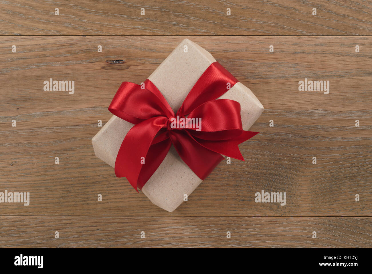 brown paper gift box with red ribbon bow on oak table Stock Photo