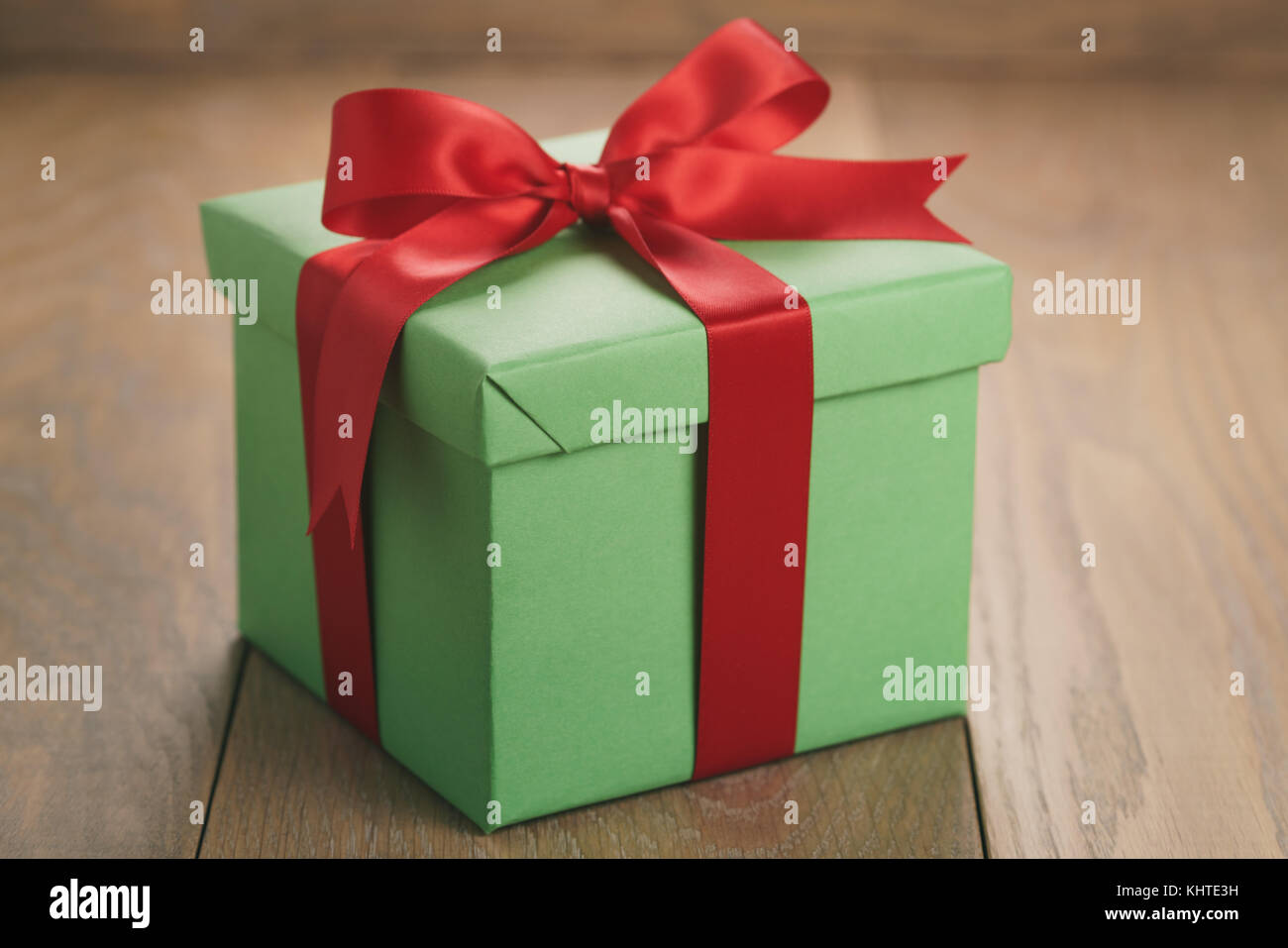 green paper gift box with red ribbon bow on oak table Stock Photo