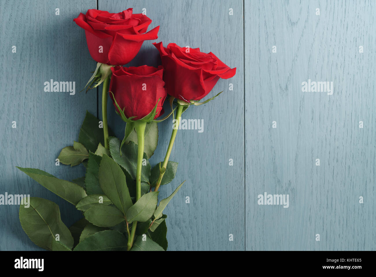 three red roses on blue wood table with copy space Stock Photo - Alamy