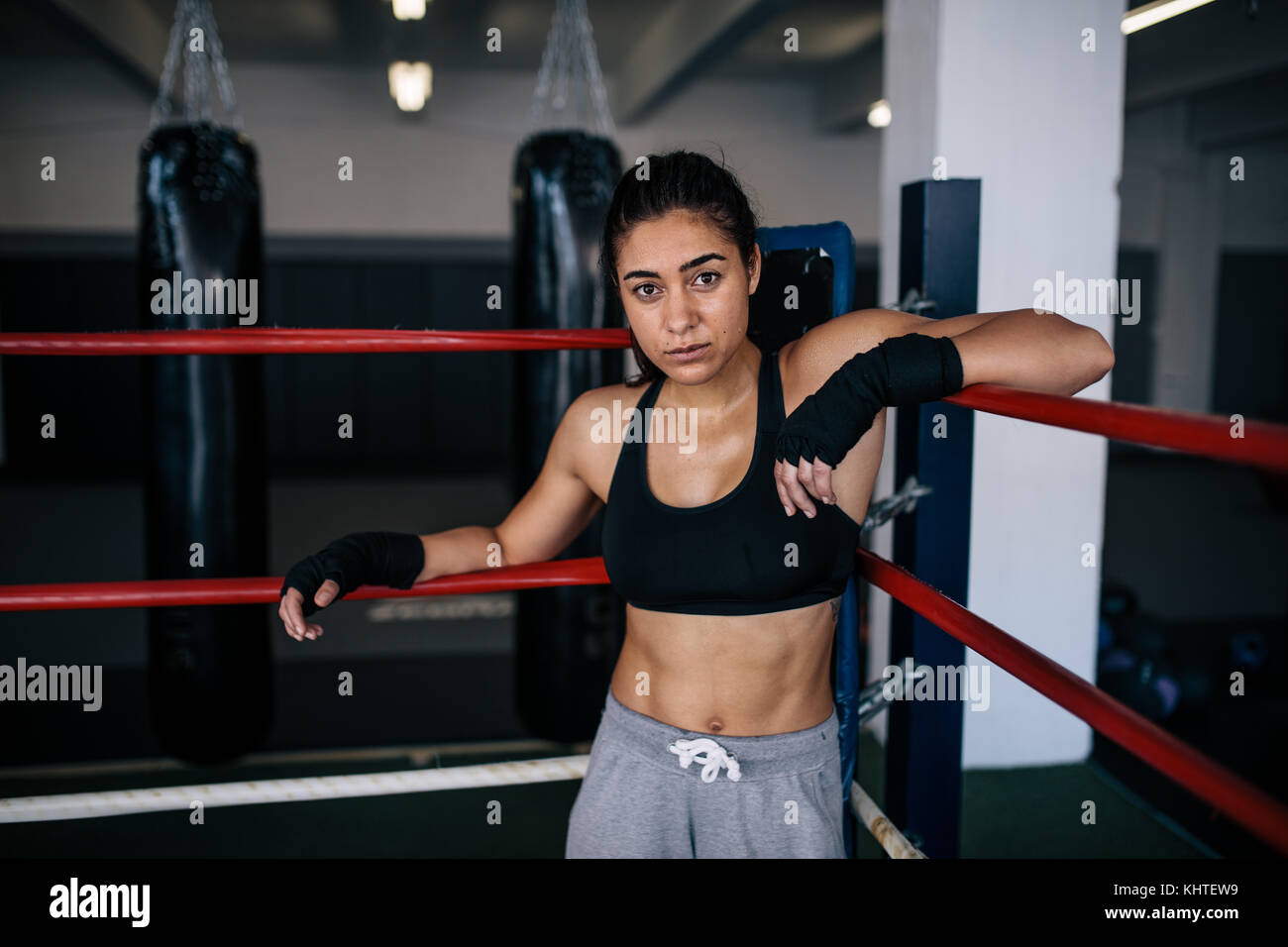 Female boxer standing inside a boxing ring with her hands resting on