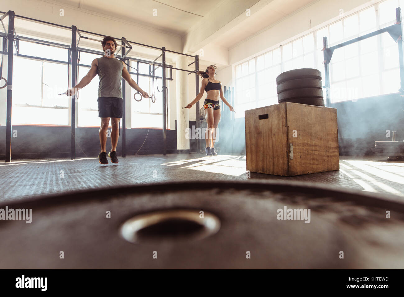 Muscular man and woman workout with jumping ropes in cross training gym. Fit young couple skipping ropes as part of their workout at health club. Stock Photo