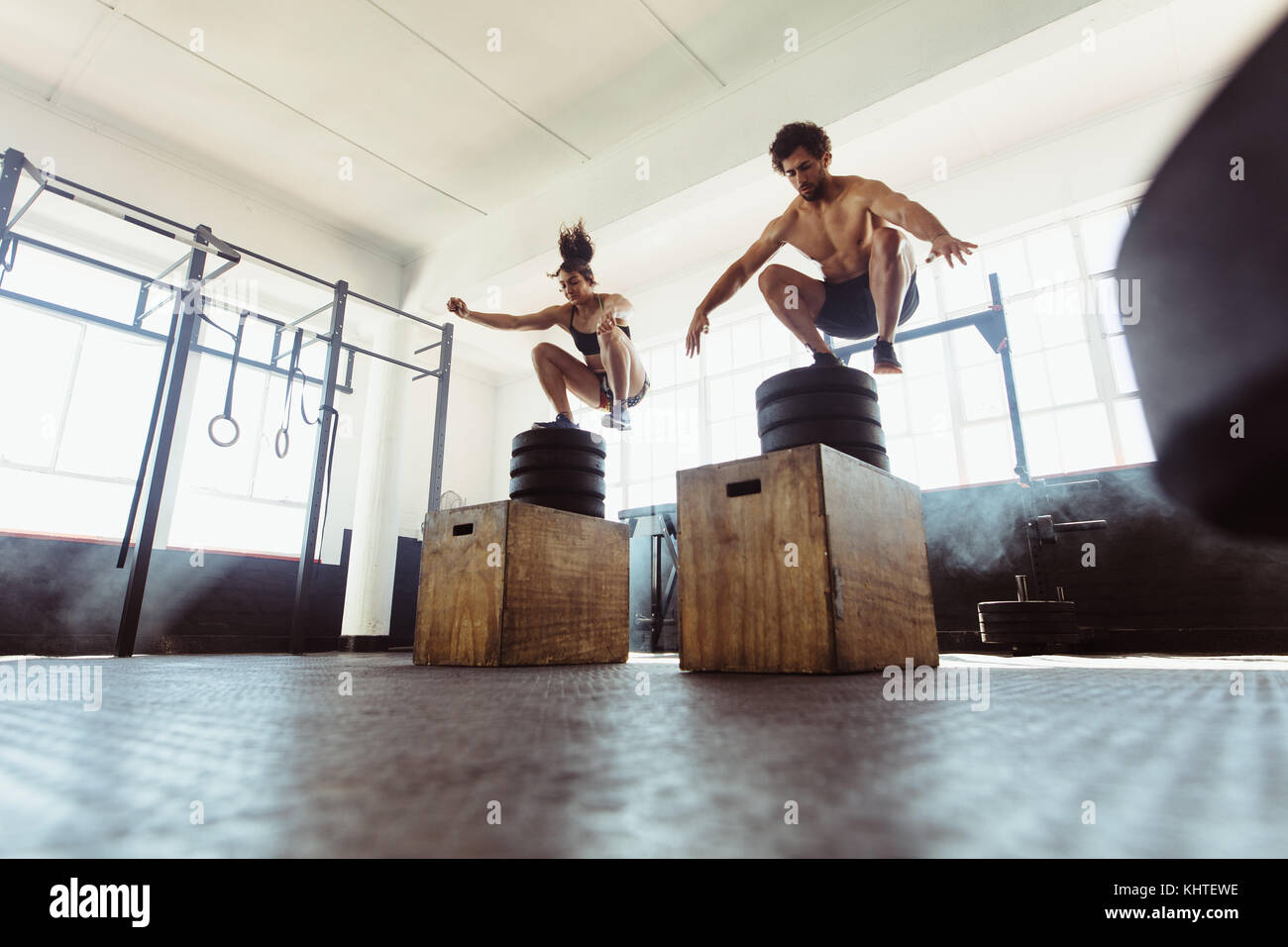 Healthy man and woman box jumping at gym. Fit young people doing cross training at health club. Stock Photo