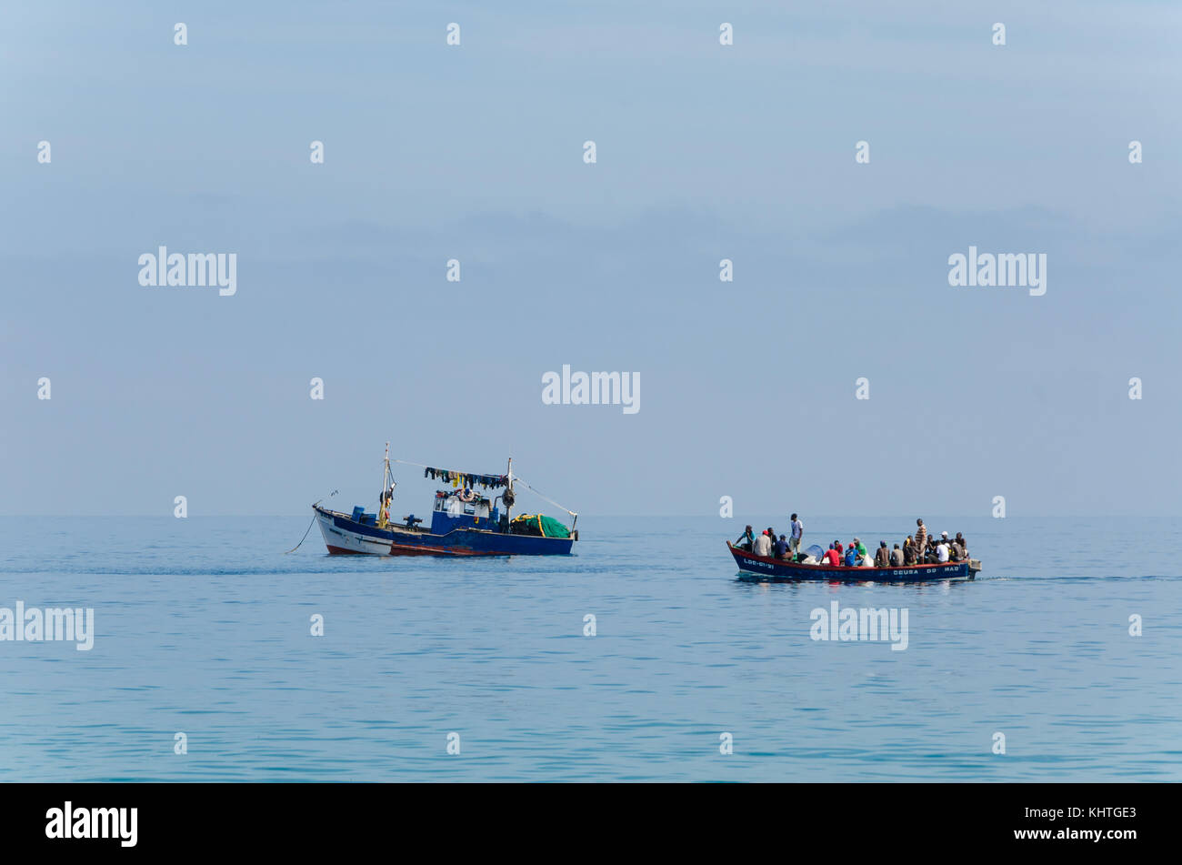 LUCIRA, ANGOLA - MAY 17 2014: Small blue painted fishing boat and smaller boat with many people on Atlantic ocean Stock Photo