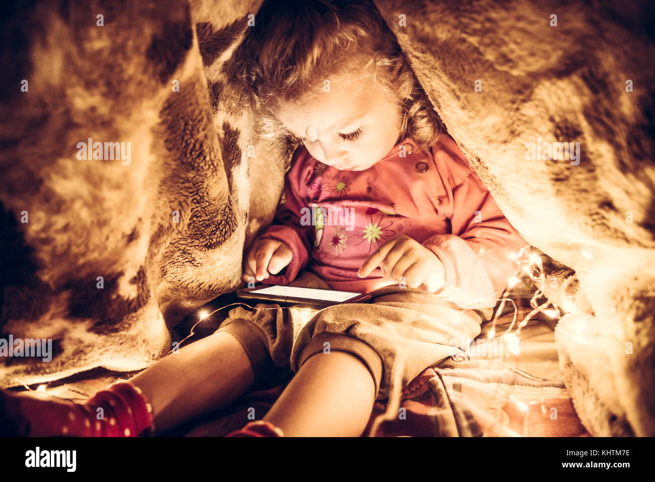 Child playing with smart phone hiding in secret place under the blanket