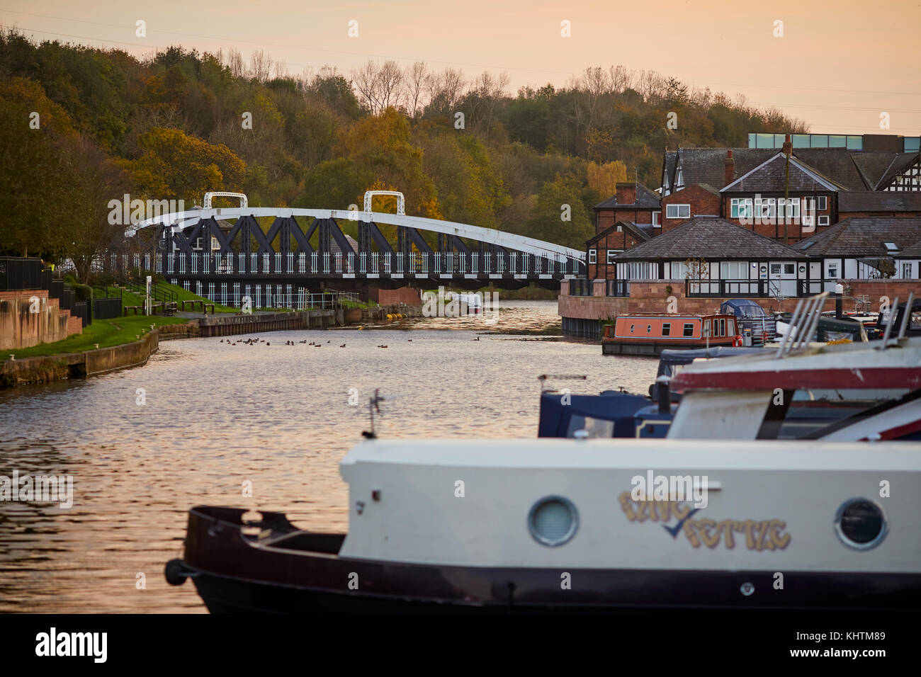 Canal boats floating on the River Weaver with golden autumn trees in the landscape and the Northwhich Town Swing Bridge in the background, Northwich i Stock Photo