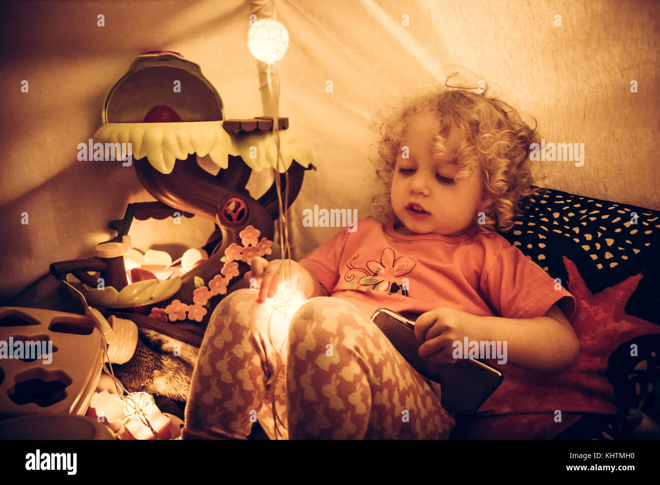 Child playing with toys in kids room in wigwam with lights with warm orange color Stock Photo
