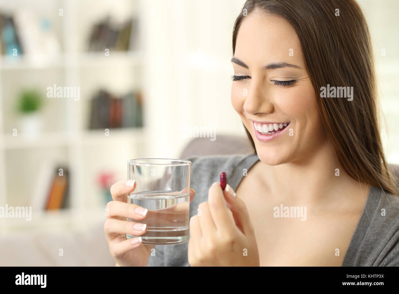 Happy lady ready to take a pill sitting on a couch at home Stock Photo