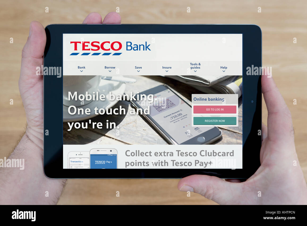 A man looks at the Tesco Bank website on his iPad tablet device, shot against a wooden table top background (Editorial use only) Stock Photo