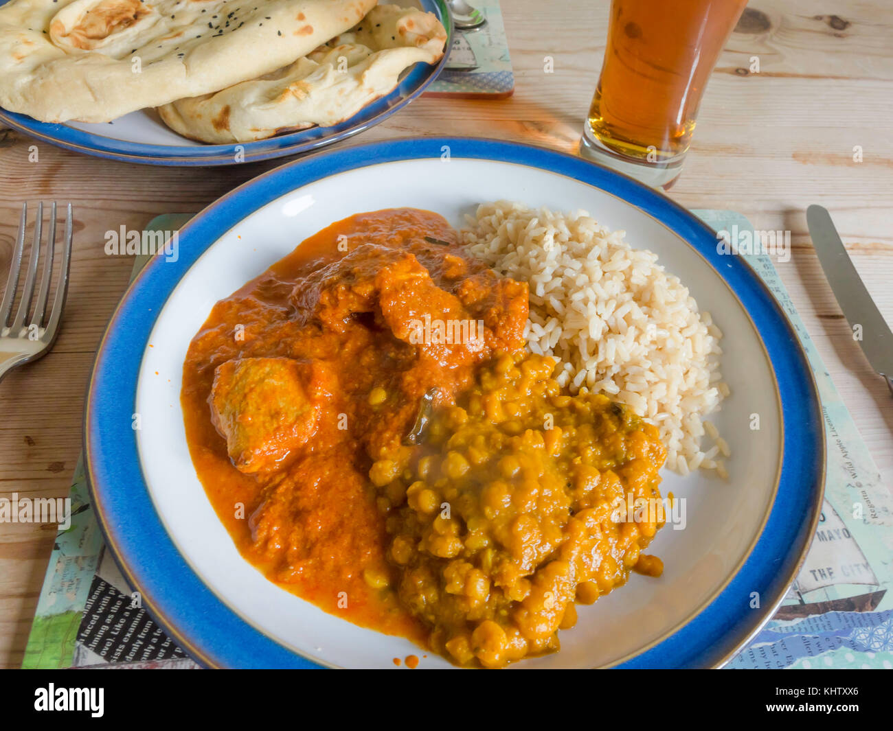 Indian Take-away food served at home Chicken Madras Curry, Tarka Dahl, Tandoori Naan Bread, Basmati Brown Rice, Mango and Lime Chutney.s and a glass o Stock Photo