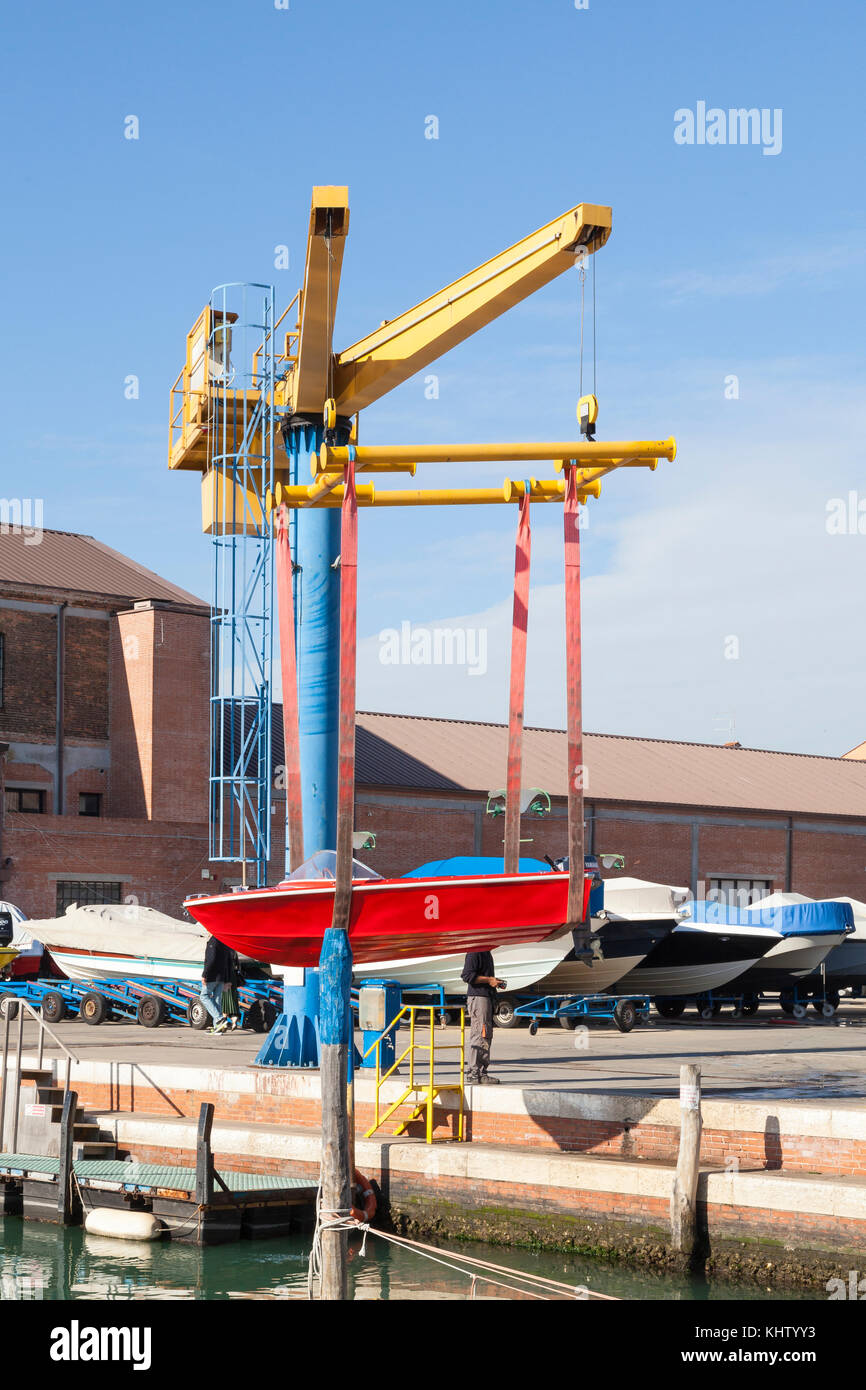 Red boat with outboard motor suspended midair in slings on a boat lift