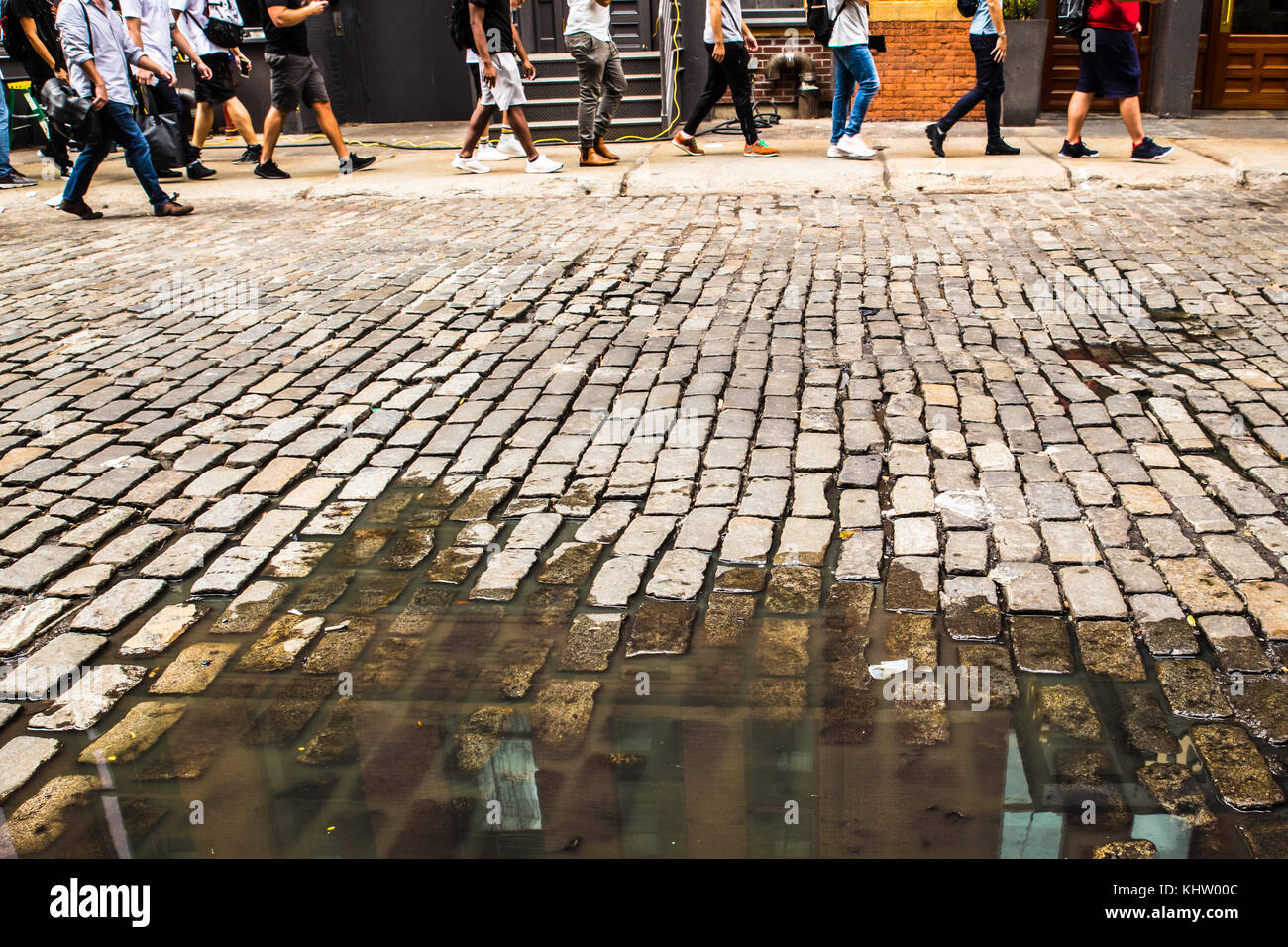 Old Cobblestone street in NYC with pedestrians and puddle Stock Photo