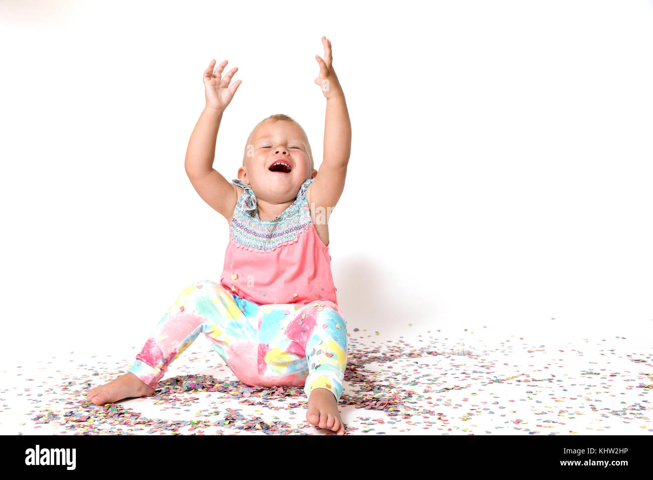 Laughing toddler girl is sitting on the floor with her arms raised ...