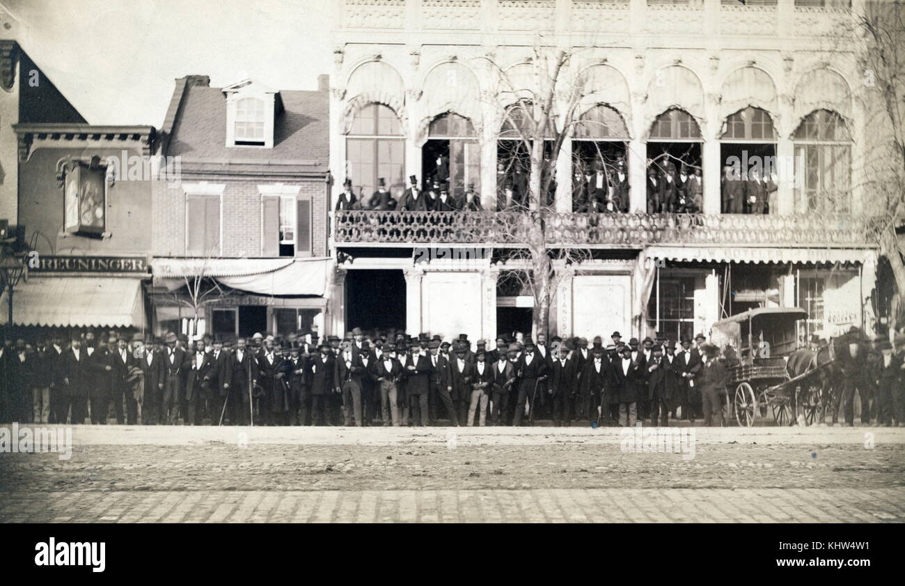 Photograph taken during the National Equal Rights Convention in Washington D.C. The photograph shows crowds of men lined along the street and on the balcony of the Metzerott Hall. Dated 19th Century Stock Photo