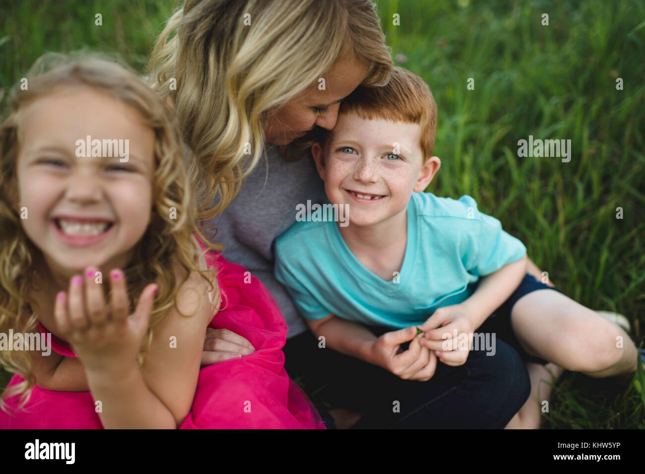 Portrait of girl and brother sitting on mothers lap in grass Stock Photo