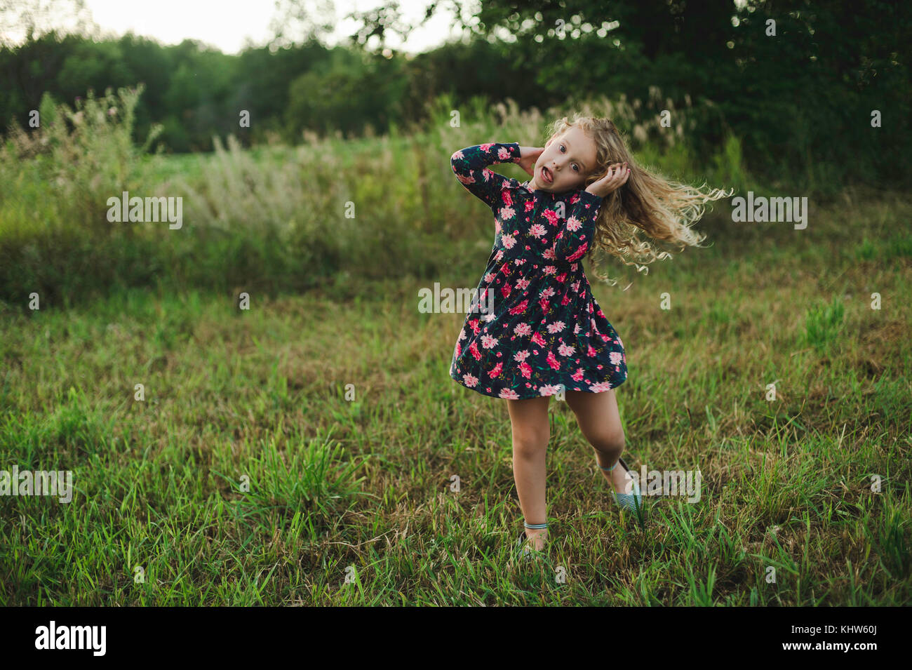 Blond haired girl running and pulling a face in field Stock Photo