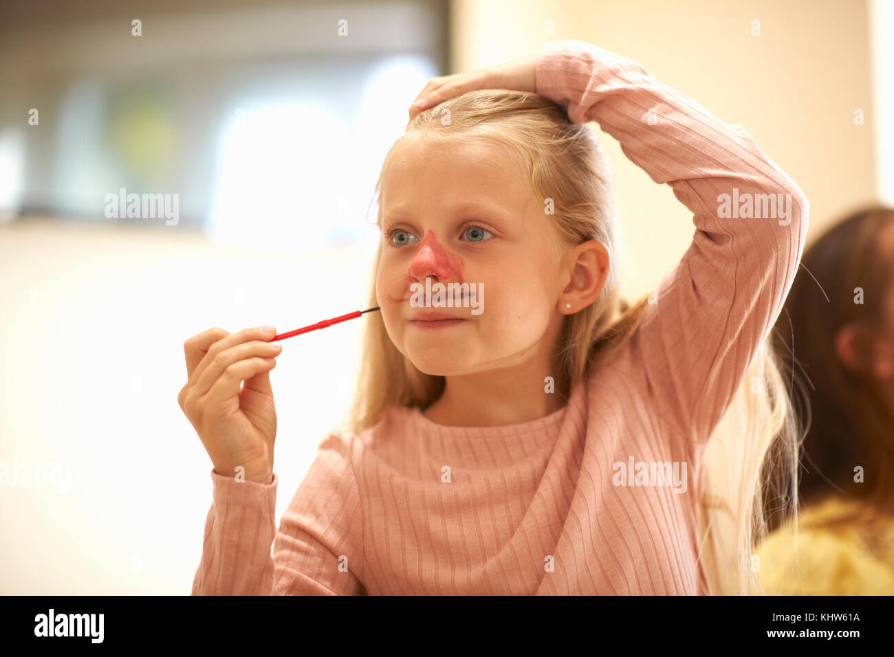 Young girl drawing on her face, using face paint Stock Photo
