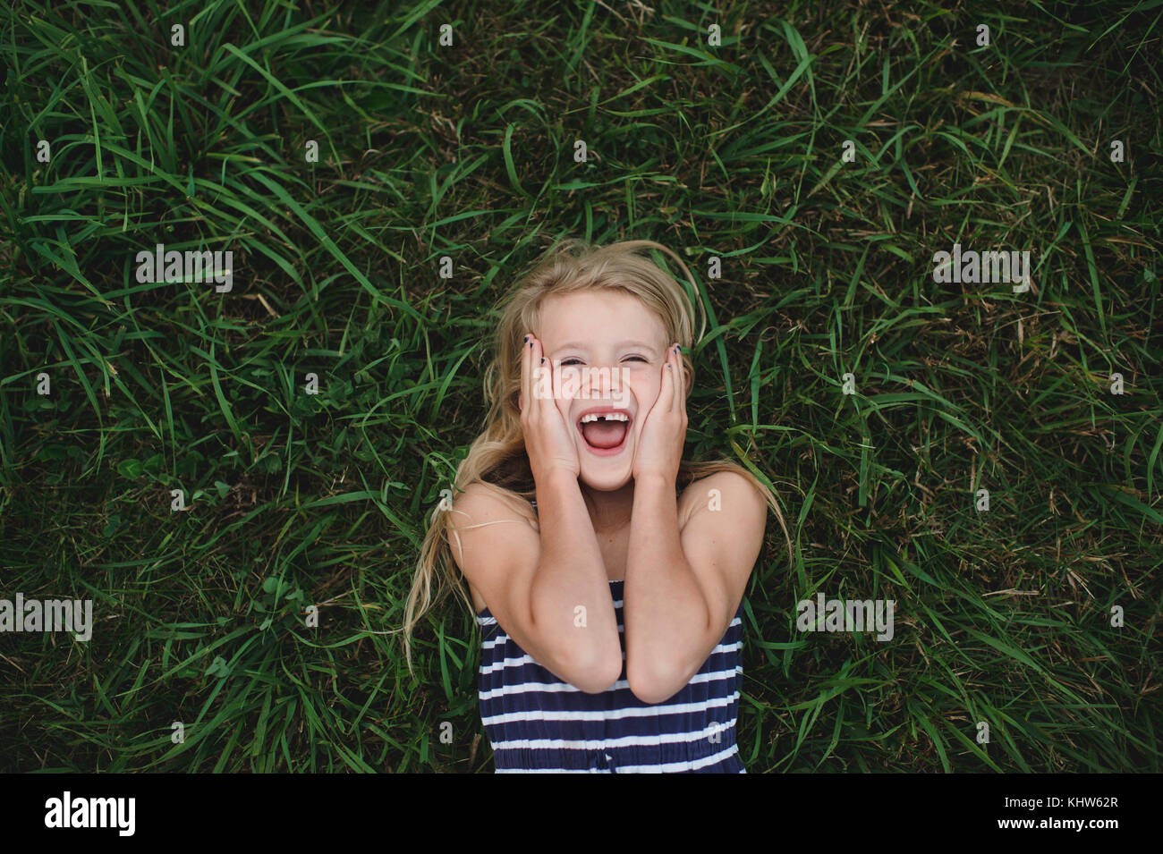 Overhead portrait of girl lying on grass with hands on her cheeks Stock Photo