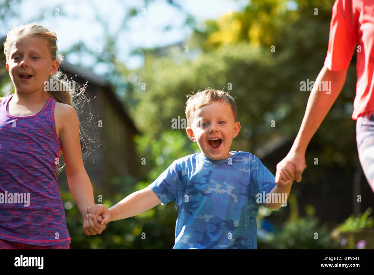 Siblings holding hands running in garden Stock Photo