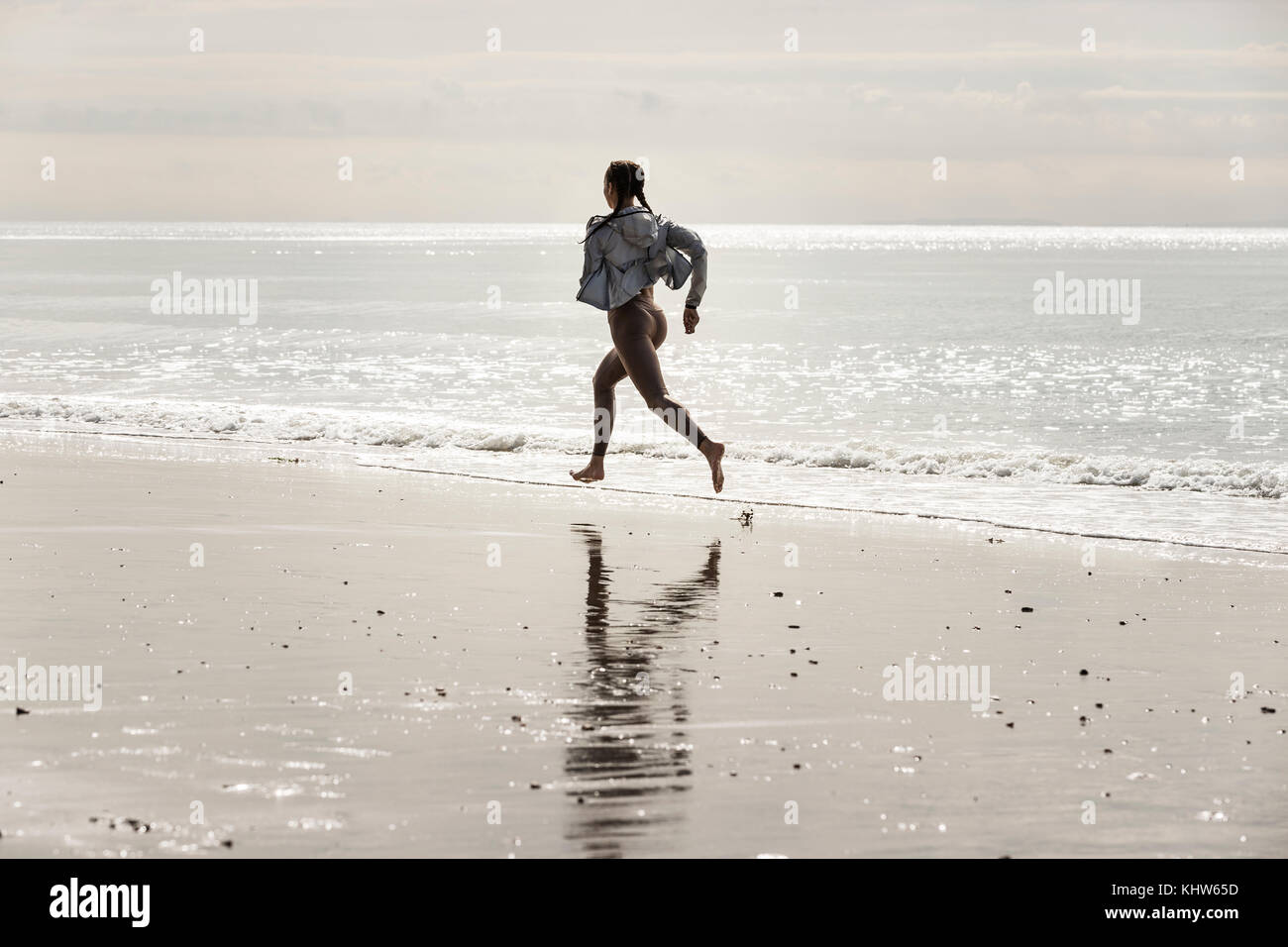 Young female runner running barefoot along water's edge at beach Stock Photo