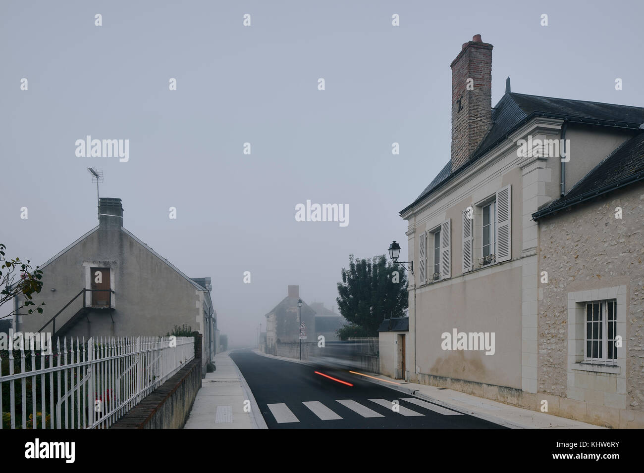 Taillight trail on road through Meigne-le-Vicomte village on misty morning, Loire Valley, France Stock Photo