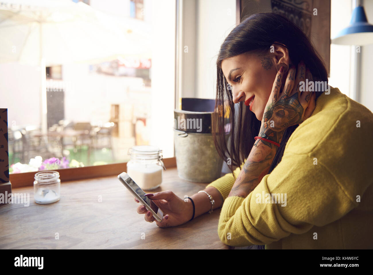 Young woman sitting in cafe, using smartphone, tattoos on arm and hand Stock Photo