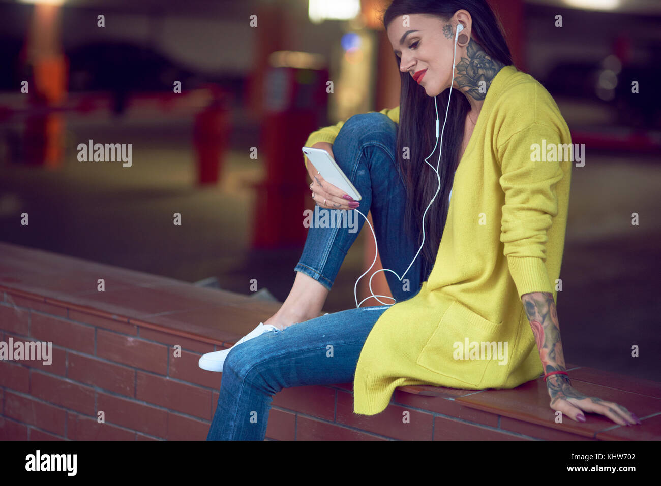 Young woman holding smartphone, wearing earphones, smiling, tattoos on hand arm, hand and neck Stock Photo