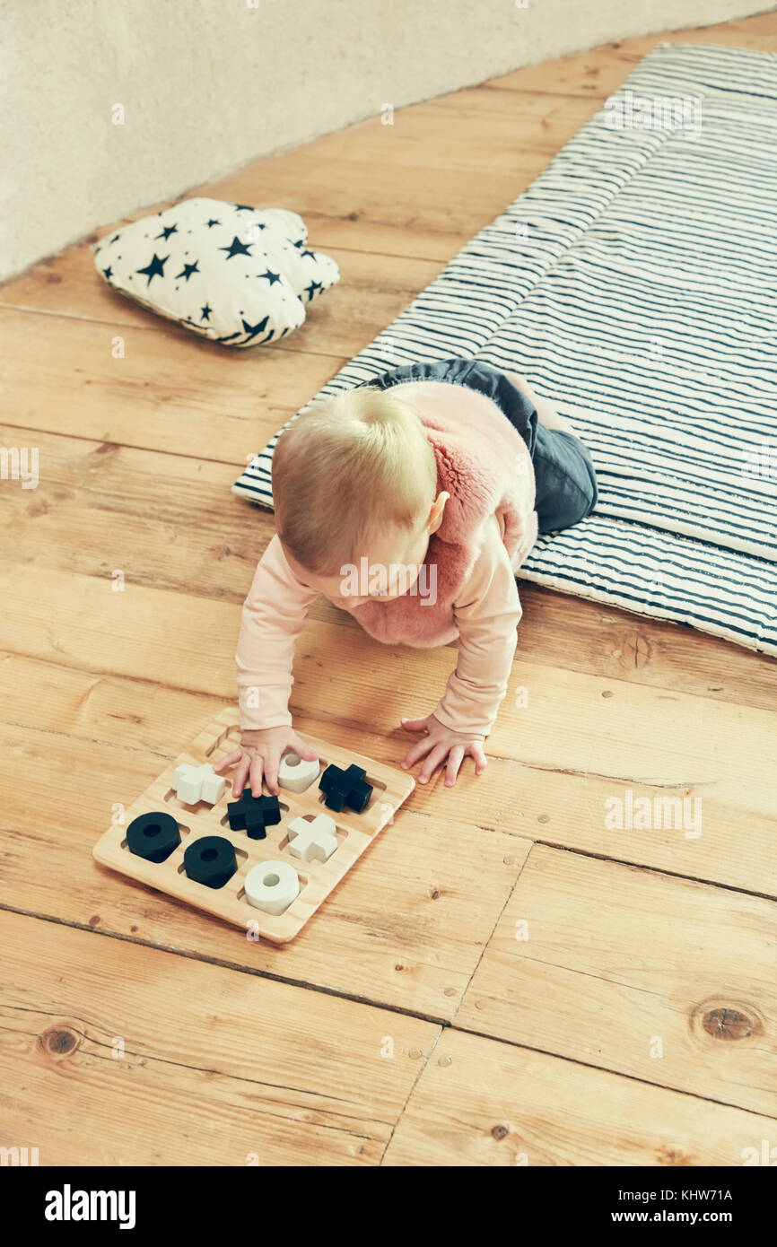 Baby girl playing with noughts and crosses on floorboards Stock Photo