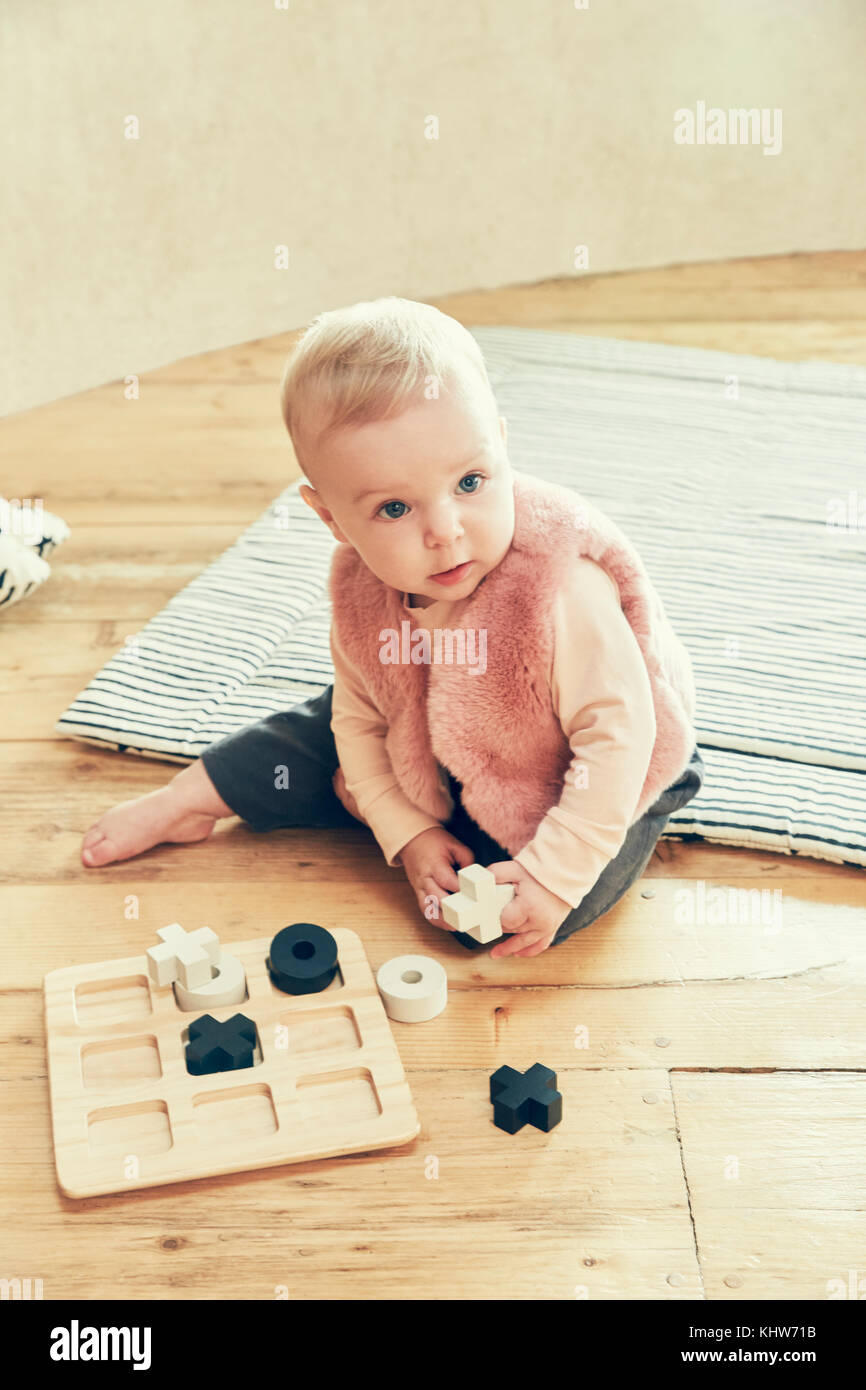 Baby girl looking away while playing noughts and crosses on floorboards Stock Photo