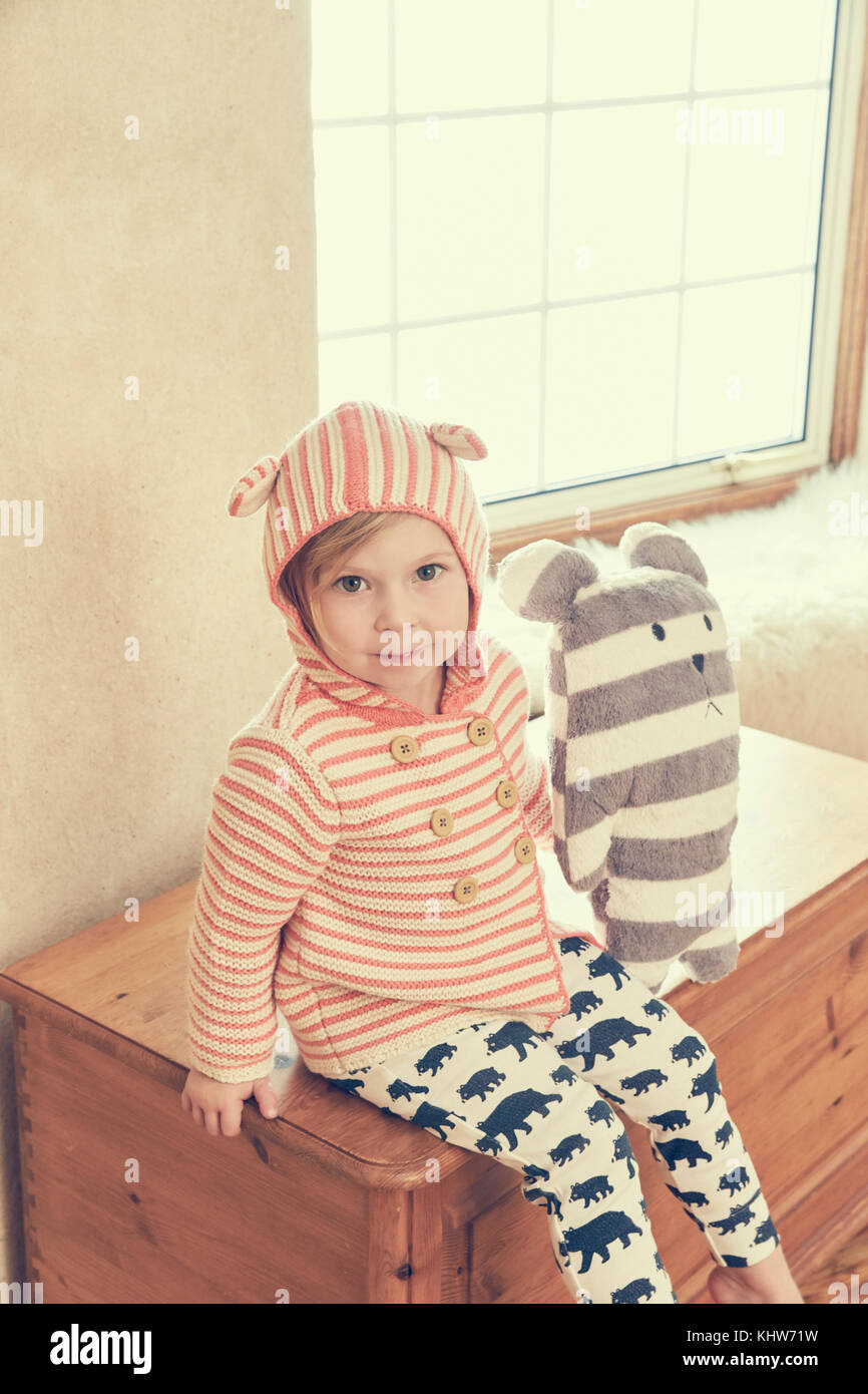 Portrait of female toddler in hood with ears sitting on ottoman Stock Photo