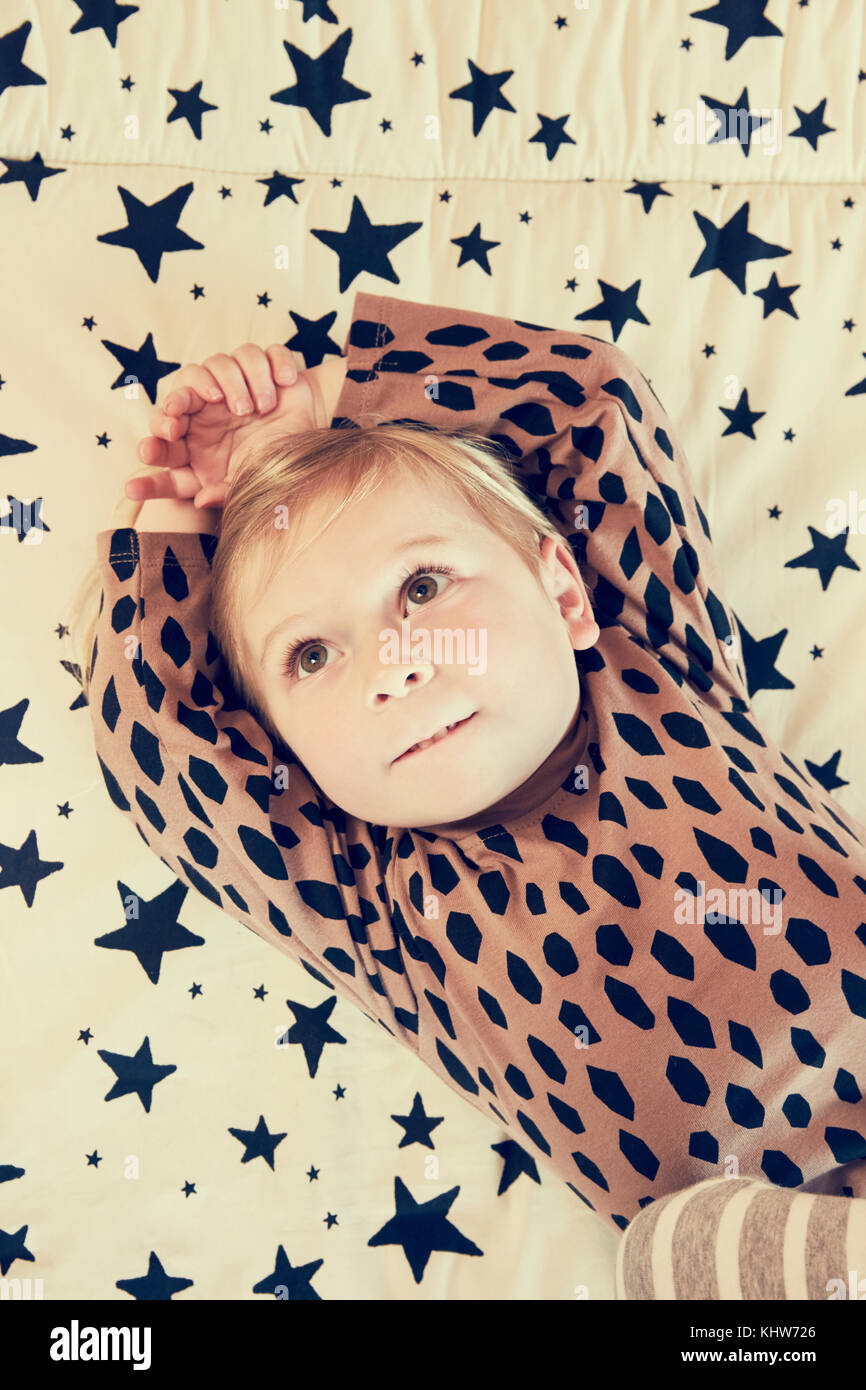 Portrait of female toddler lying on star pattern bed looking upward Stock Photo
