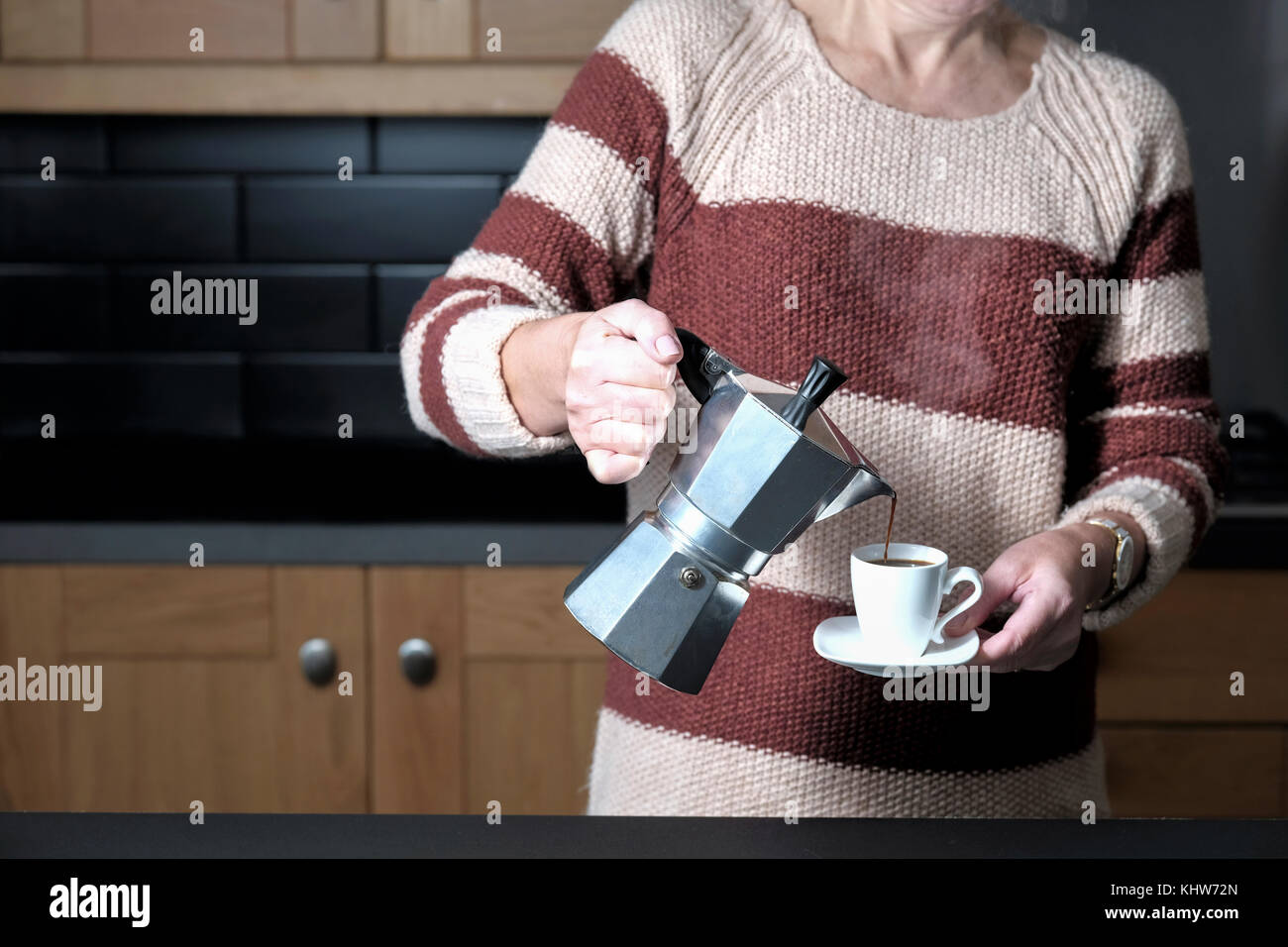 A smart but casually dressed woman pouring an espresso coffee from a molar hob espresso maker