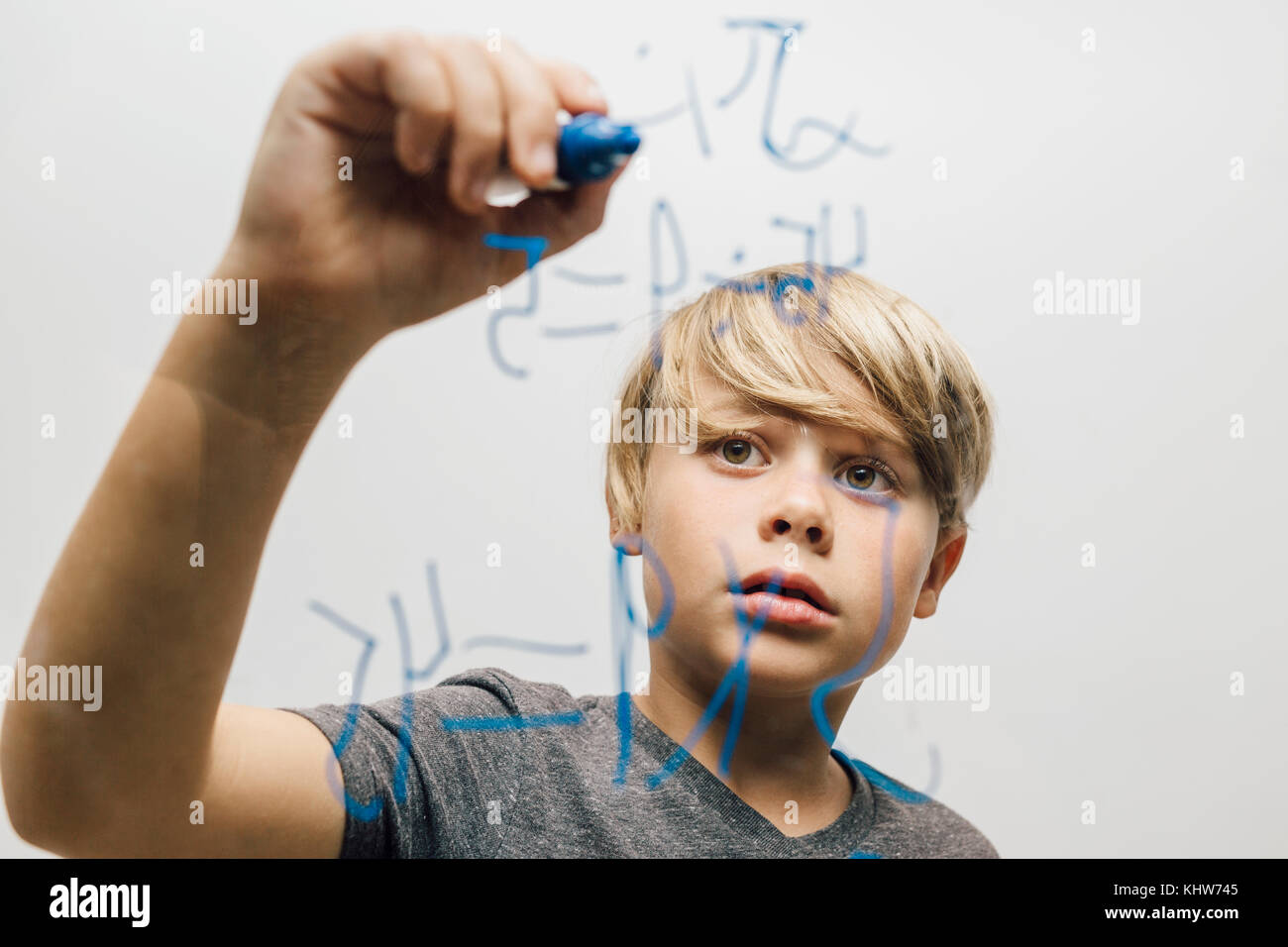 Close up of boy's hand writing equation onto glass wall Stock Photo