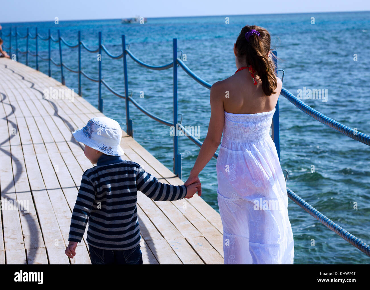 Rear view of girl strolling along sea pier hand in hand with brother Stock Photo