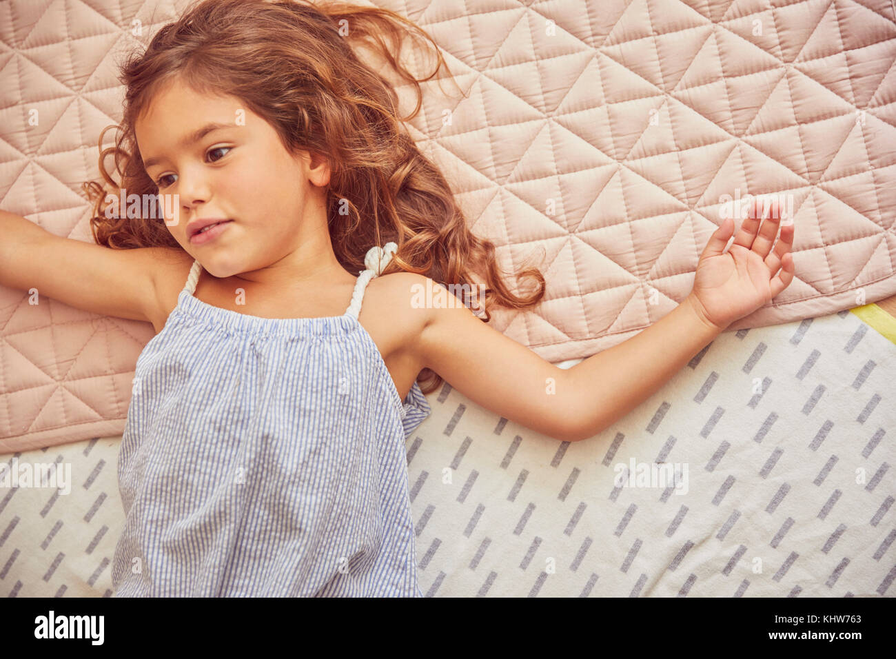 Young girl lying on bed, thoughtful expressions, overhead view Stock Photo