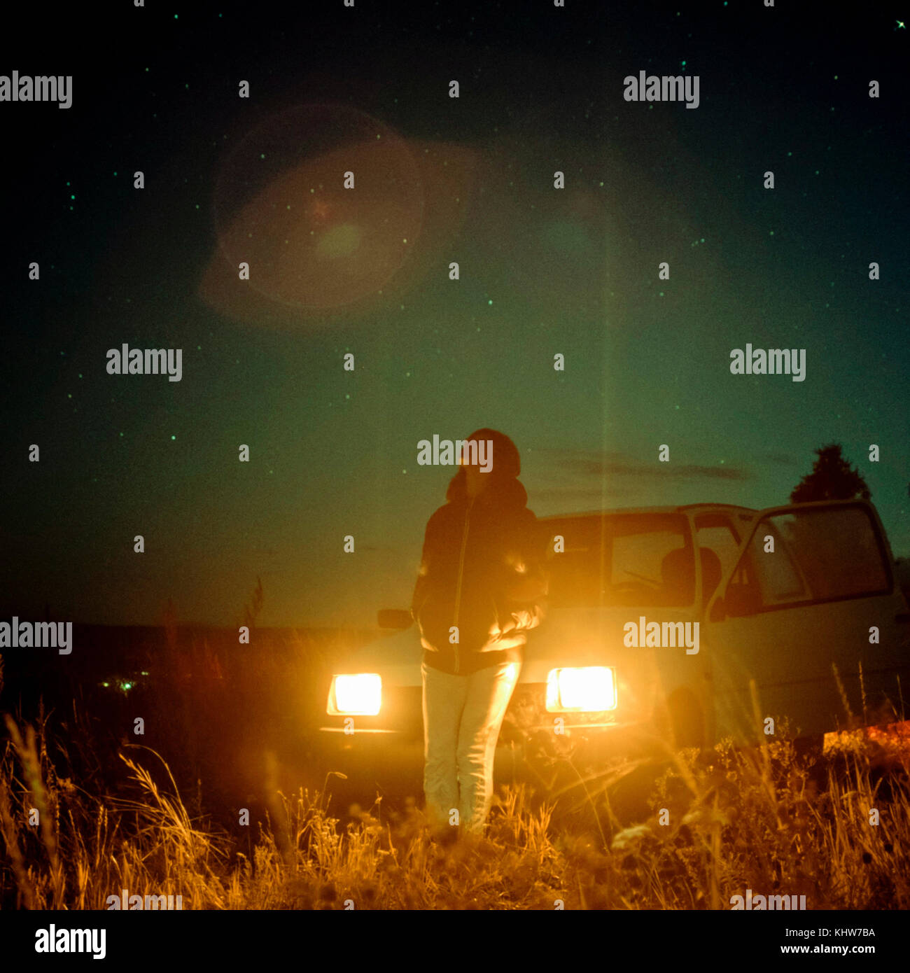 Woman in rural setting at night, leaning against car, headlights illuminated, Ural, Sverdlovsk, Russia, Europe Stock Photo