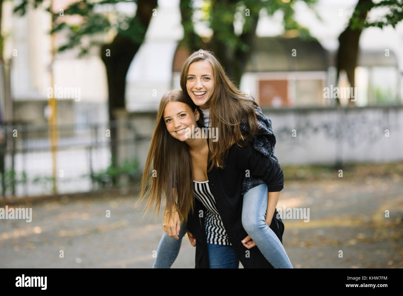 Portrait of young woman giving best friend a piggy back in park Stock Photo
