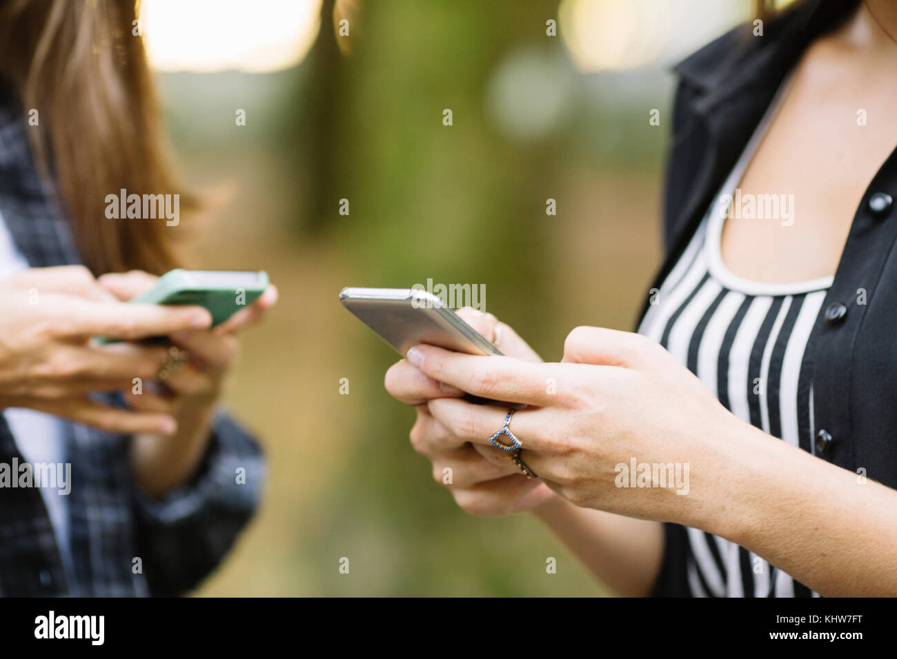 Cropped shot of two young women using smartphone touchscreen in park ...
