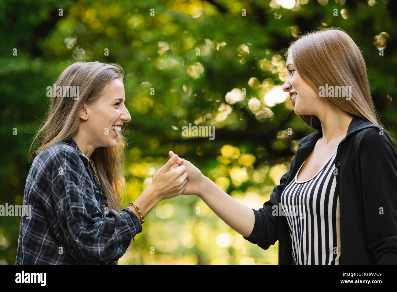 Two young female friends giving secret handshake in park Stock Photo