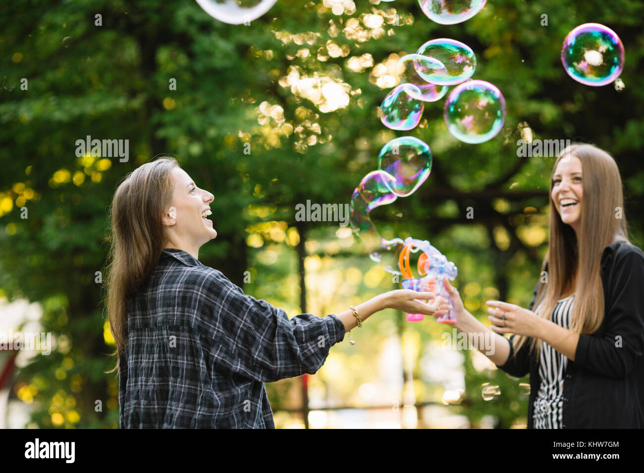 Two young female friends making floating bubbles in park Stock Photo