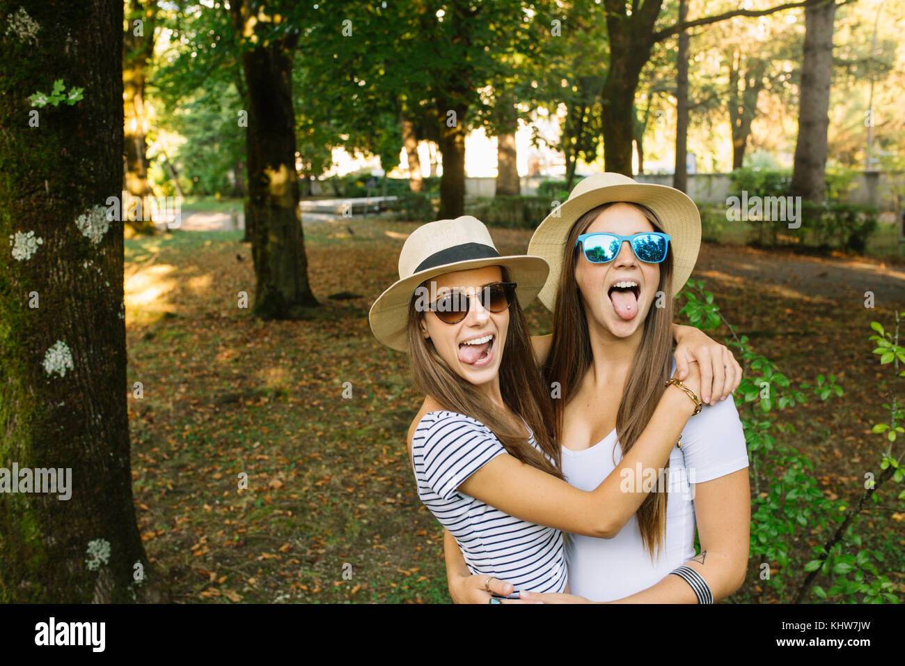 Portrait of two young female friends in trilby hats sticking out tongues in park Stock Photo