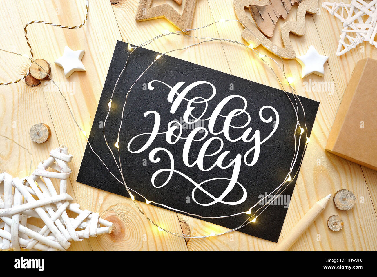 Christmas text Holly Jolly on a chalkboard with christmas deoccrusties star, garland on wooden background. Flat lay, top view photo mockup Stock Photo