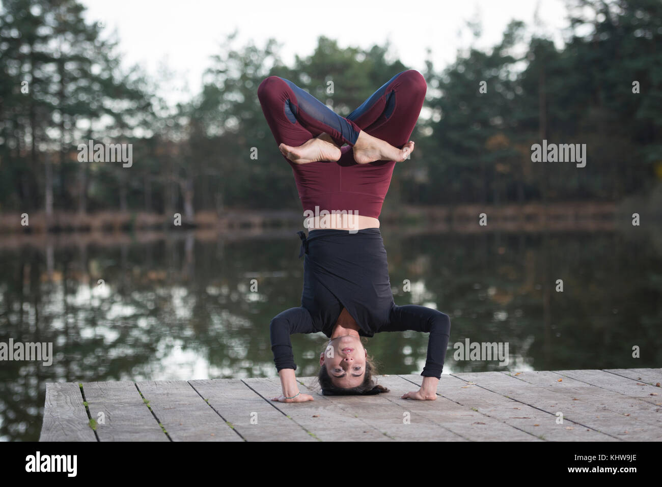 woman practicing yoga by a lake doing a headstand with crossed legs. Stock Photo
