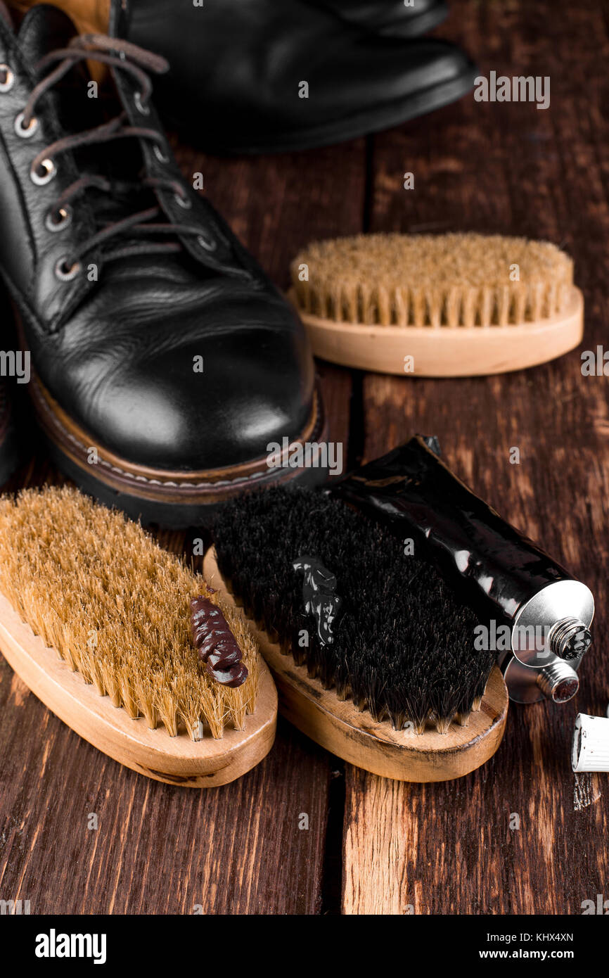 Black boots on wooden background with polishing equipment, brush and