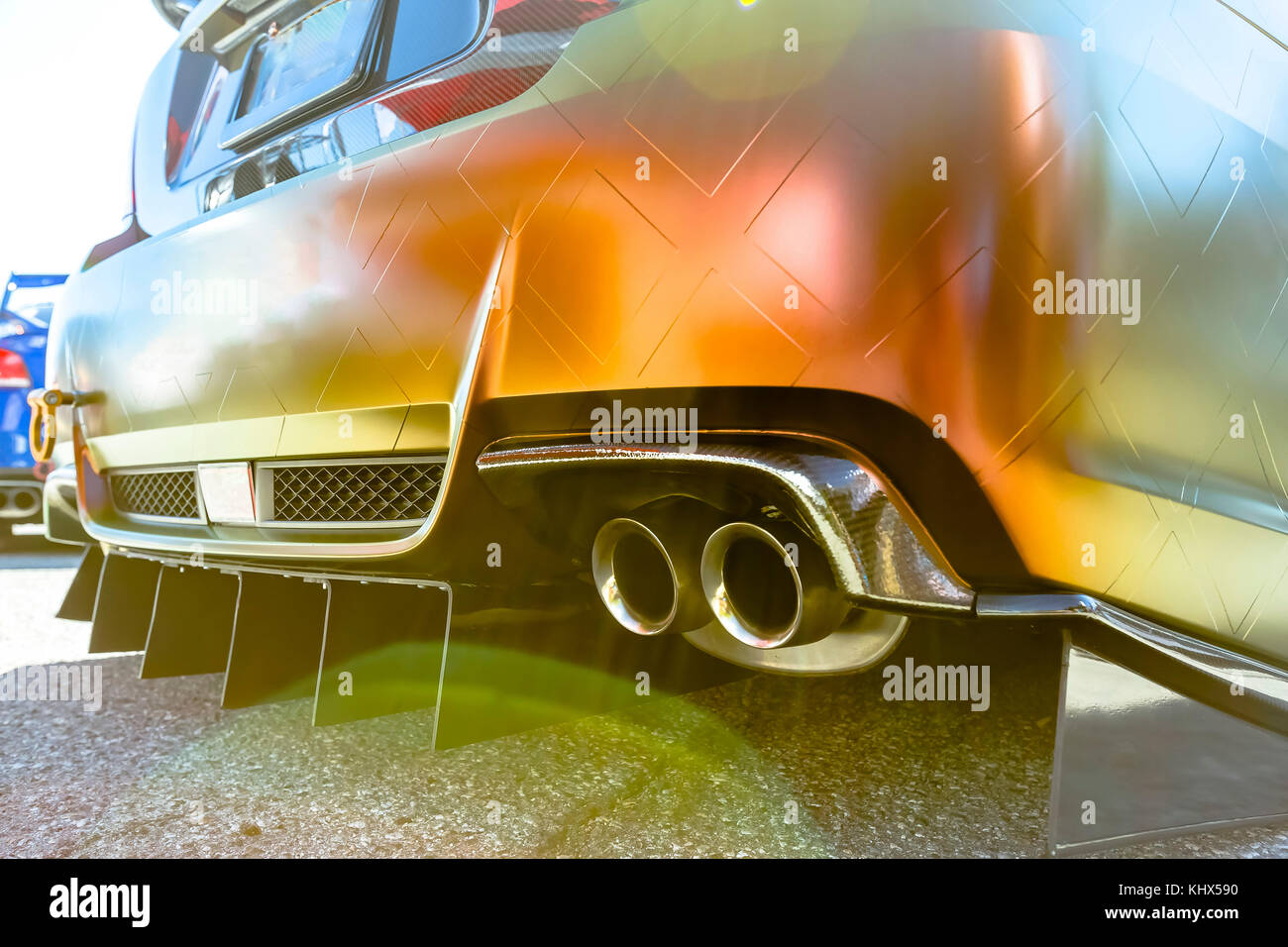 Orange car with dual exhaust pipes on concrete with lens flair. Custom cars in Southern