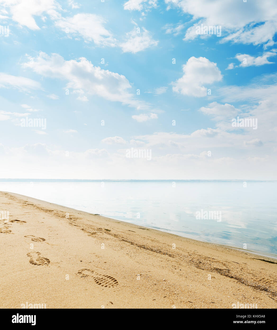 Yellow sand on riverside and footprint in it. Clouds in blue sky over ...